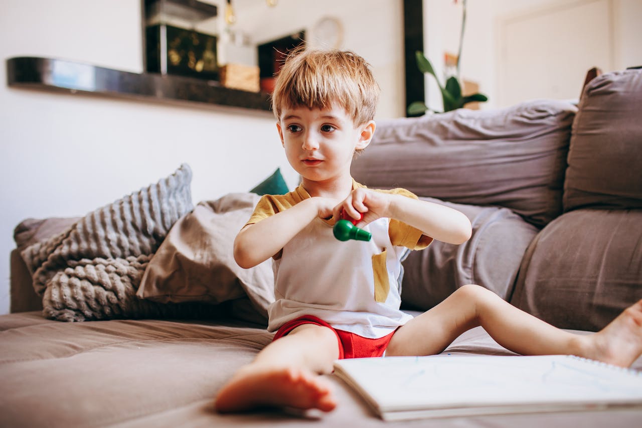 Mastering the First Impression: Your intriguing post title goes here A child sits on a couch at home, playfully holding a toy and surrounded by a cozy living room setting.