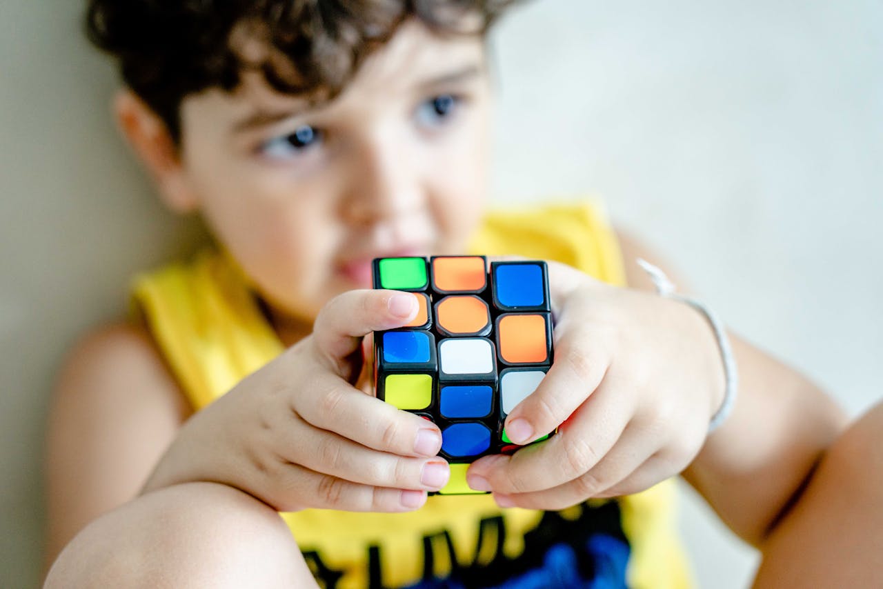 services-02 Young boy holding and concentrating on solving a colorful Rubik's Cube indoors.