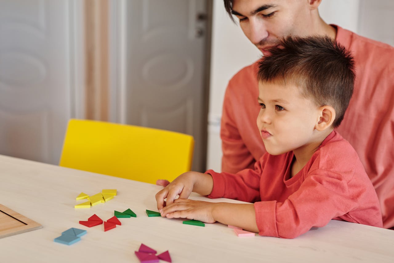 A father and son enjoy a bonding activity indoors, playing with colorful tangrams together.