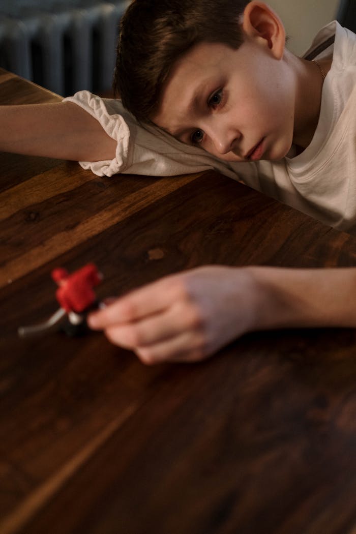 gallery-5 A thoughtful child plays with a toy at a wooden table, conveying a sense of introspection.