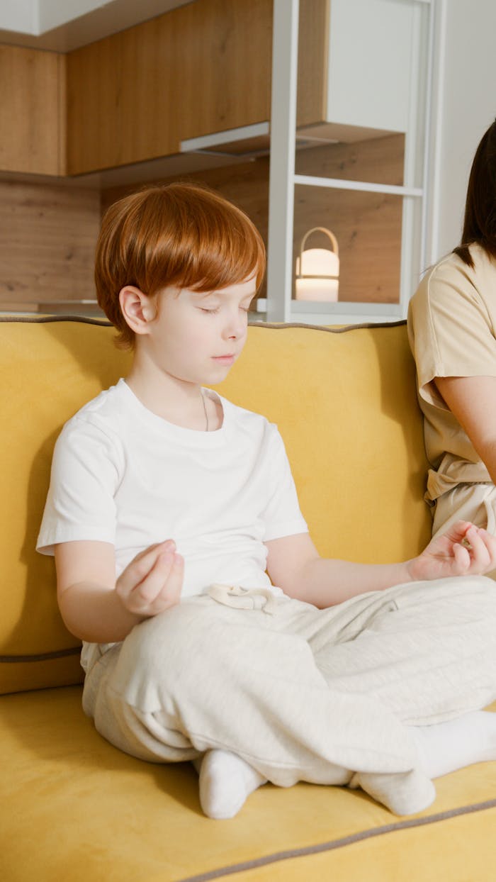 hero-img-02 Young redheaded boy practicing meditation on a yellow couch at home.