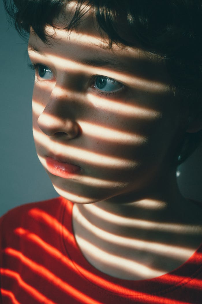 Crafting Captivating Headlines: Your awesome post title goes here A child's face is dramatically lit by striped shadows, evoking a sense of innocence and introspection.