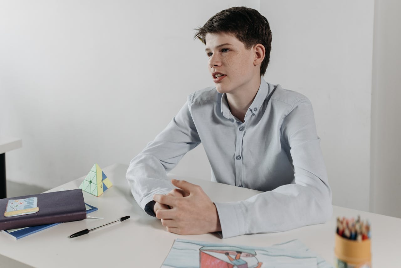 The Art of Drawing Readers In: Your attractive post title goes here Boy sitting at a desk in a classroom, surrounded by books and drawings, looking thoughtful and engaged.