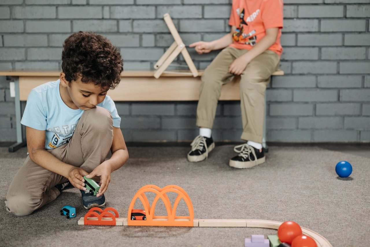 Two kids enjoying creative play with wooden toy tracks in a classroom setting.