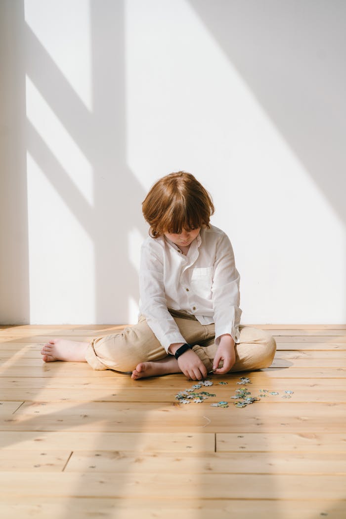 services-04 Young boy focuses on assembling a puzzle on wooden floor indoors.